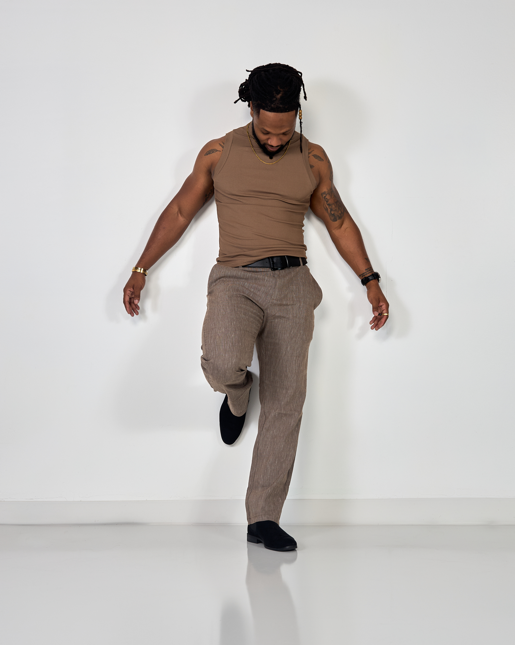 a male wearing a brown outfit posing against a white wall.