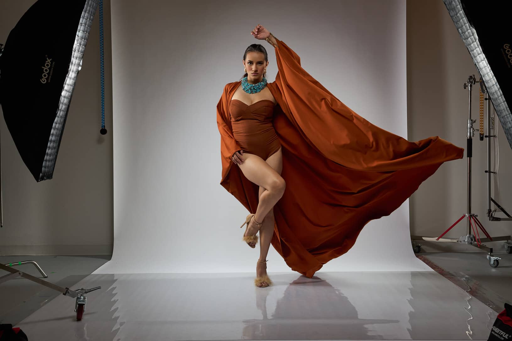 A bold visual statement in rich burnt orange, Paula wears a voluminous draped cape that transforms into a sculptural silhouette. Paired with statement jewelry and a sleek ponytail, this editorial look channels high-art elegance and Afro-modern fashion influence.